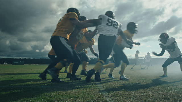 American Football Field: Two Professional Teams Clash, Trying to Score Touchdown Points. Defense and Offense Brutally Compete for the Ball, Tackle Each other. Dramatic Cinematic Slow Motion Shot