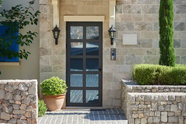 Photo of Modern house facade with stone finished wall, glass door and bushes in europe