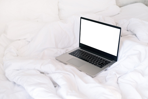 workspace in bed. Laptop  in bed on clean white linens. Work at home concept. Mock-up