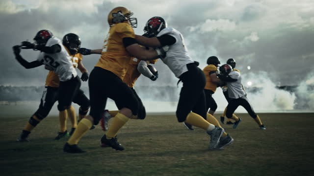 American Football Field Two Teams Play: Successful Player Jumping Over Defense Running to Score Touchdown Points. Professional Athletes Compete for the Ball, Fight for Victory. Dramatic Slow Motion