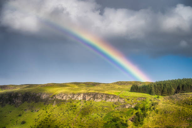 Closeup on rainbow arching over hills and forests covered in patches of sunlight, Glenariff Forest Park Closeup on vivid rainbow arching over hills and forests covered in patches of sunlight, Glenariff Forest Park, County Antrim, Northern Ireland glenariff photos stock pictures, royalty-free photos & images
