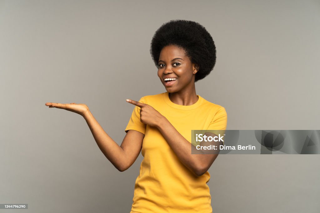 Happy excited female point finger to open palm with empty space for product placement happy smiling Overjoyed excited female point finger on open palm with empty space for product advertisement happy smiling. Black young woman advertising service or business with cheerful satisfied emotional face Women Stock Photo