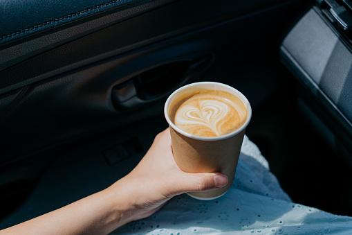 Image of an Asian woman holding a take away coffee in car