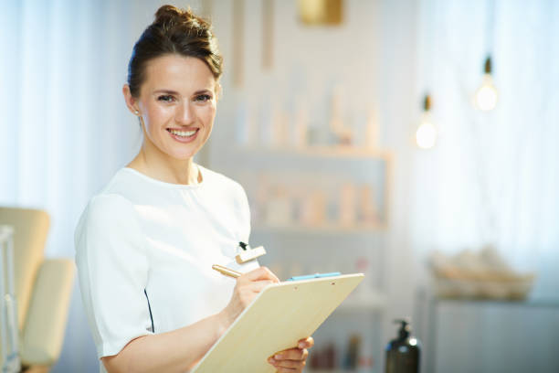 employée souriante avec presse-papiers dans un studio de beauté moderne - moisturizing cream audio photos et images de collection