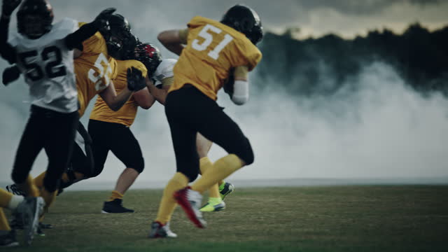 American Football Field Two Teams Compete: Successful Player Jumping Over Defense Running to Score Touchdown Points. Professional Athletes Compete for the Ball, Tackle, Fight for Championship Victory