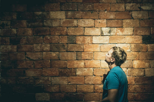 Side view man under life crisis problems stand facing looking on brown brick wall left up corner, wants to climb, overcome obstacle, reach a goal, leader, motivation.