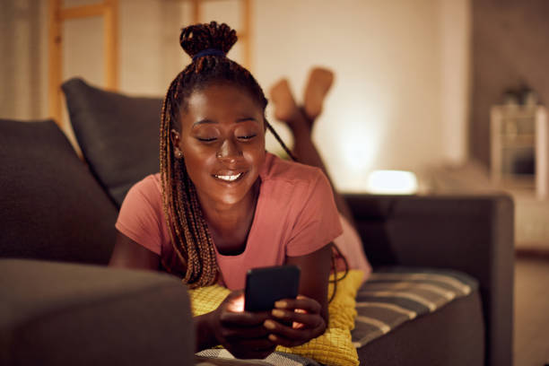 istock Happy African American woman text messaging on cell phone while relaxing on the sofa. 1344803705
