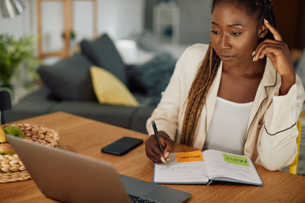 istock Young black woman reading an e-mail on laptop and writing notes while working at home. 1344803784