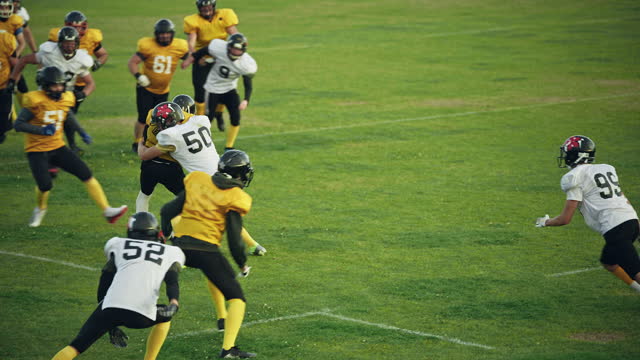 American Football Teams Start Game: Professional Players, Aggressive Face-off, Tackle, Pass, Fight for Ball and Score. Warrior Competition Full of Brutal Energy, Power, Skill. Slow Motion Wide Shot