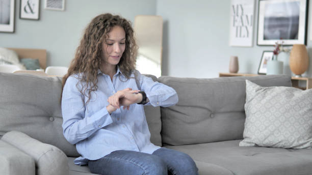 istock Curly Hair Woman Using Smartwatch while Sitting on Sofa 1344811496
