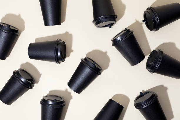 Black closed paper cups for coffee and tea, on a beige background, top view