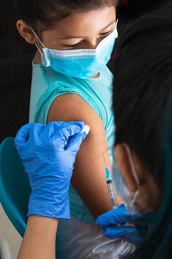children's nurse disinfecting brown girl's arm before administering injection. doctor injecting covid-19 vaccine. flu vaccine. medical concept, health and pandemic.