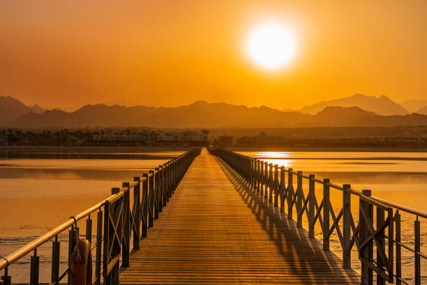 산과 바다 물 위에 밝은 오렌지 일몰로 이어지는 나무 다리 도로 - boardwalk pontoon bridge landscape sky 뉴스 사진 이미지