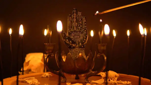 Photo of Fortune teller hand or palmistry on the witch table with animal bones. Palmistry with black palm and candles in the candelabra. Magic alchemy spirituality symbol. Palm reading in mystic, occult room.