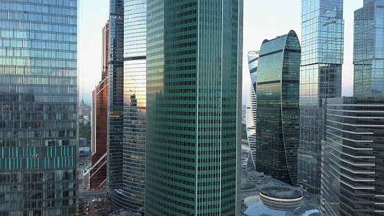 Camera rising among the high-rise office buildings in city business centre. Modern skyscrapers at sunset