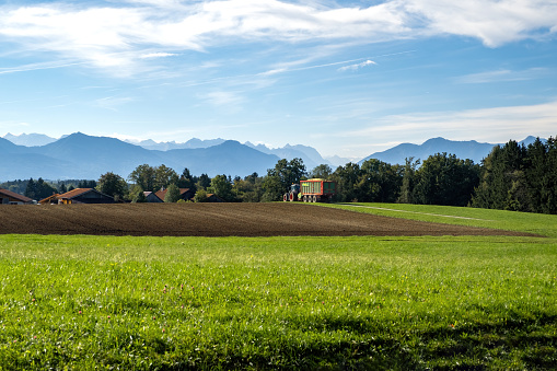 harvested bavarian field in autumn, with mountains in the background and a tractor driving home.
