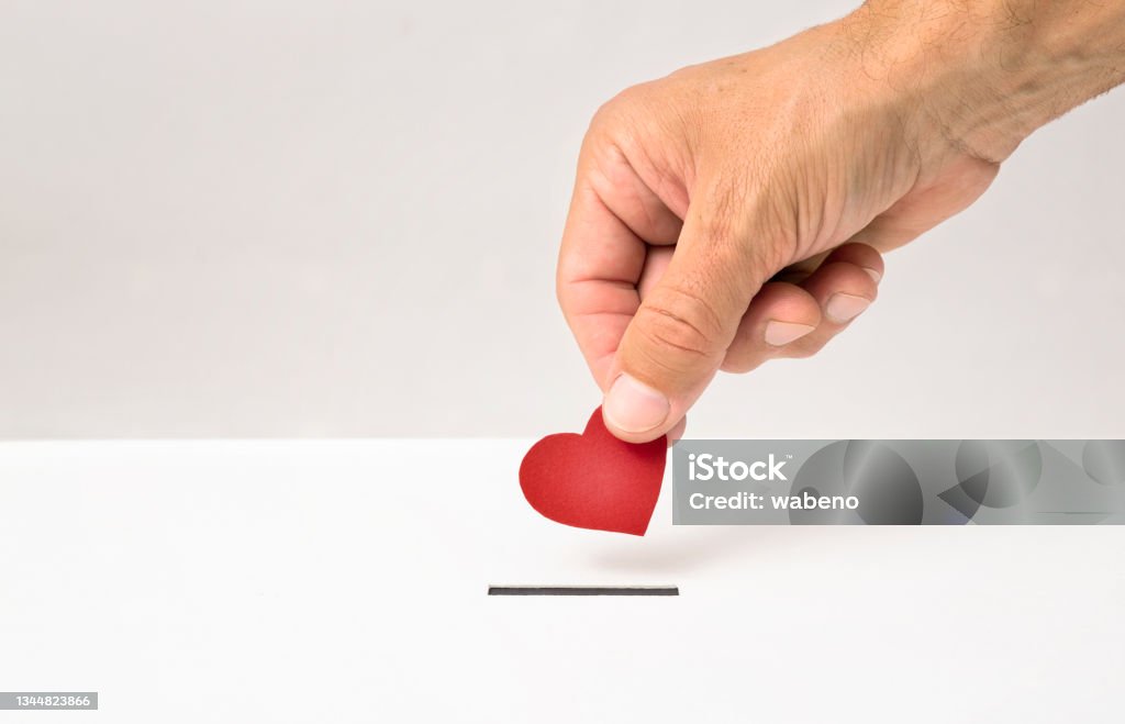 Red heart symbol is put by person's hand into slot of white donation box Red heart symbol is put by person's hand into slot of white donation box, Concept of donorship, life saving or charity Organ Donation Stock Photo