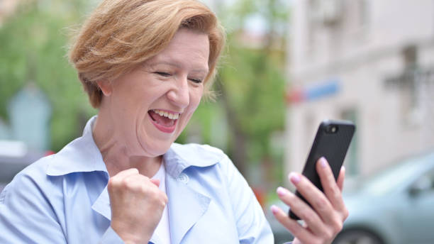 istock Outdoor Old Woman Excited for Success while Using Smartphone 1344824138