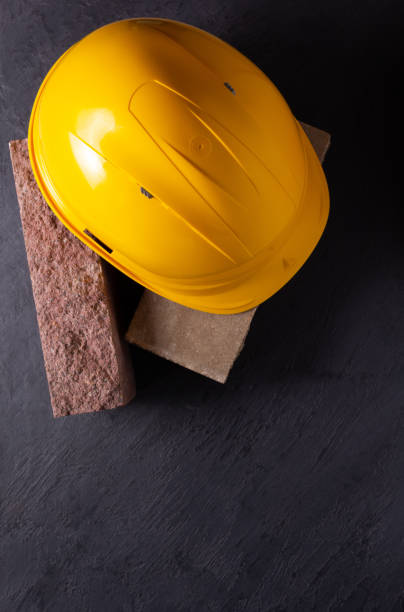 istock Construction hardhat on brick at black slate stone background. Helmet and bricks 1344825877