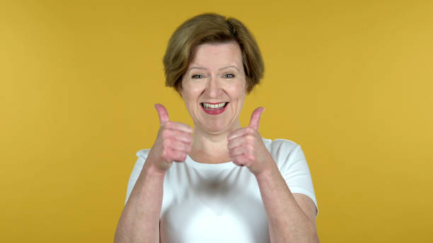 istock Old Woman Gesturing Thumbs Up Isolated on Yellow Background 1344826704