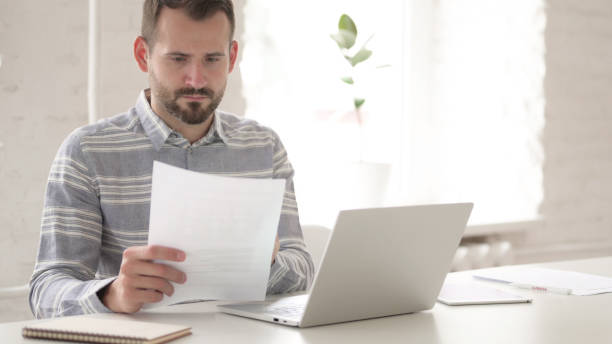 istock Casual Young Man Doing Paperwork and Typing on Laptop 1344827163