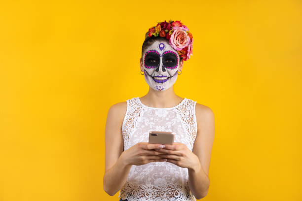 mexican catrina, portrait of young latin woman holding mobile phone for halloween party in mexico - face paint human face mask carnival imagens e fotografias de stock