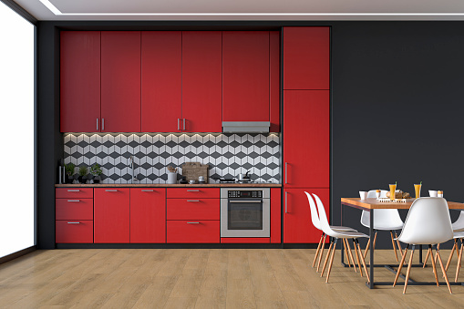 Empty modern kitchen with fire red high wooden kitchen cabinets with tiled pattern background,  ceiling led lights, dining table and  chairs. A large black plaster wall background on hardwood floor with copy space and windows on a side. 3D rendered image.
