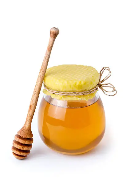 A jar of sweet flower honey with honeycomb lid and wooden dipper