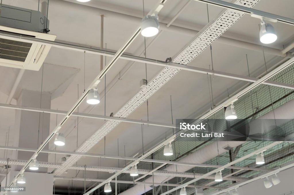 Ceiling with bright lights in a modern warehouse, shopping center building, office or other commercial real estate object. Directional LED lights on rails under the ceiling Illuminated Stock Photo