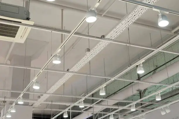 Photo of Ceiling with bright lights in a modern warehouse, shopping center building, office or other commercial real estate object. Directional LED lights on rails under the ceiling