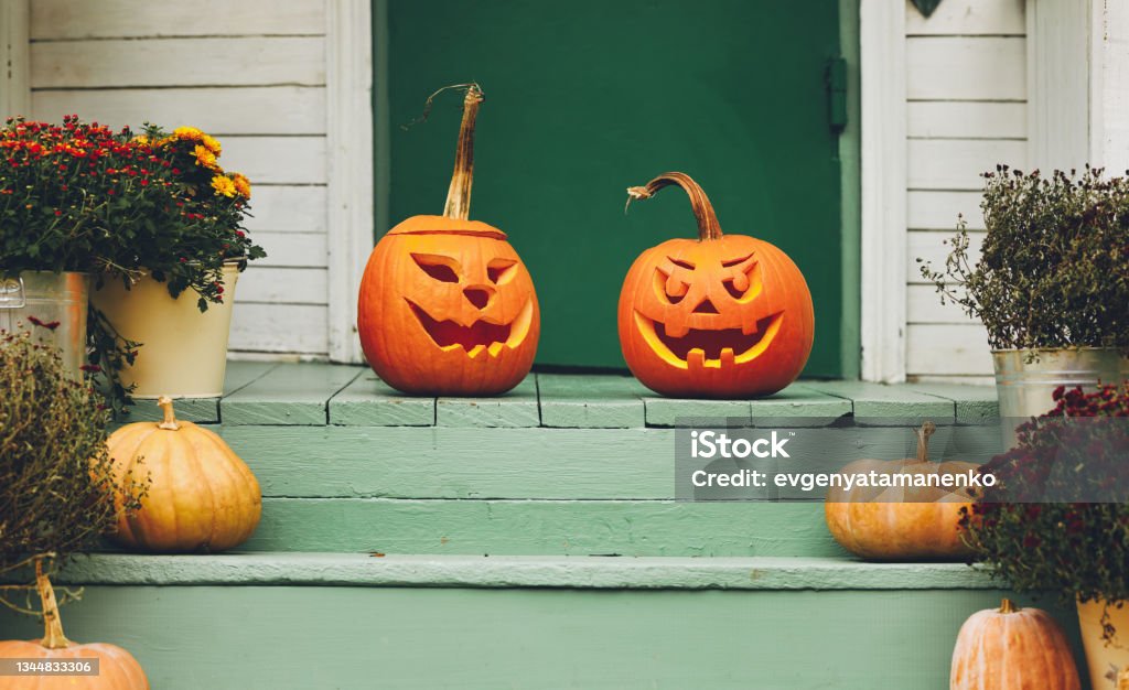 House with halloween orange pumpkin decoration, jack o lanterns with spooky faces on porch Staircase autumn decor. House entrance with halloween pumpkin decoration on wooden stairs, two jack o lanterns with spooky faces on porch of apartment building during all hallows eve Jack O' Lantern Stock Photo