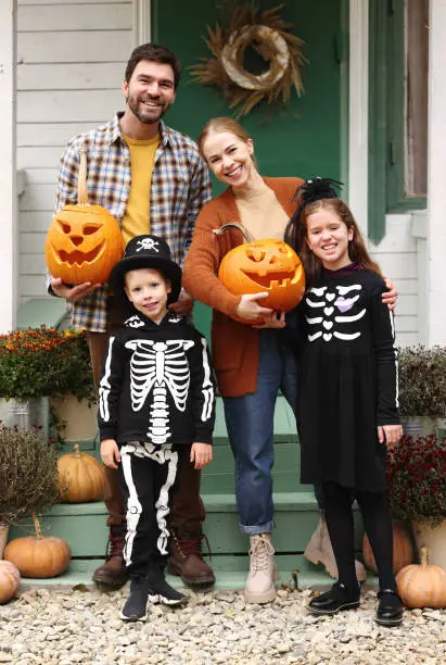 Photo of Young happy family parents with kids standing on house porch during Halloween holidays
