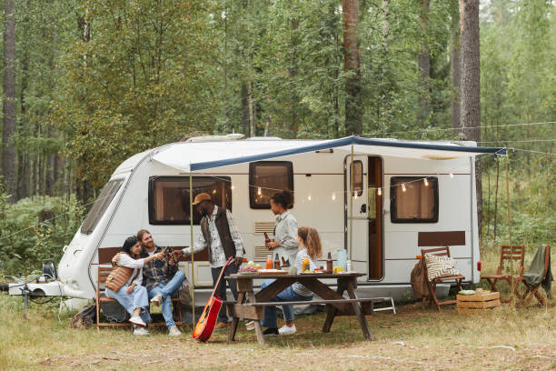 Group of Friends Relaxing by RV Van Wide angle view of young people enjoying outdoors while camping with van in forest, copy space manufactured housing stock pictures, royalty-free photos & images