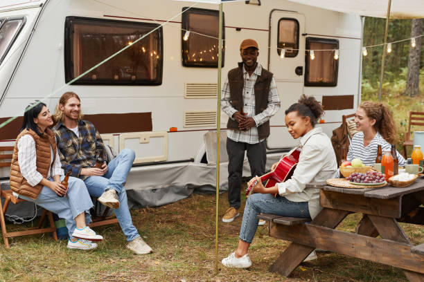 Young People Playing Guitar Outdoors Full length portrait of young African-American woman playing guitar while enjoying camping outdoors with diverse group of friends rv stock pictures, royalty-free photos & images