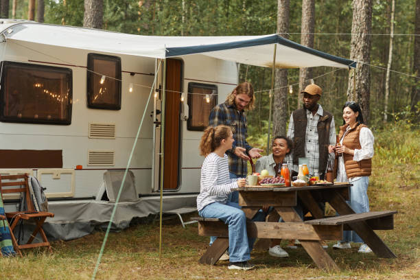 Modern Young People Camping in Autumn Wide angle view at diverse group of young people enjoying picnic outdoors while camping with trailer van, copy space fall picnic table stock pictures, royalty-free photos & images