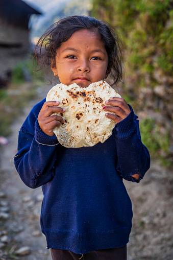 Nepali little girl eating chapati for a breakfast, village in Annapurna Conservation Area. Chapati is a Indian flatbread, made of whole wheat flour known and mixed into dough with water and optional salt.