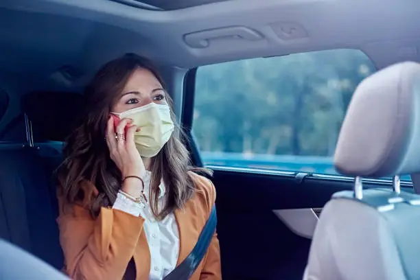 Caucasian woman with a face mask wearing her cell phone in a car - Business woman talking on her cell phone