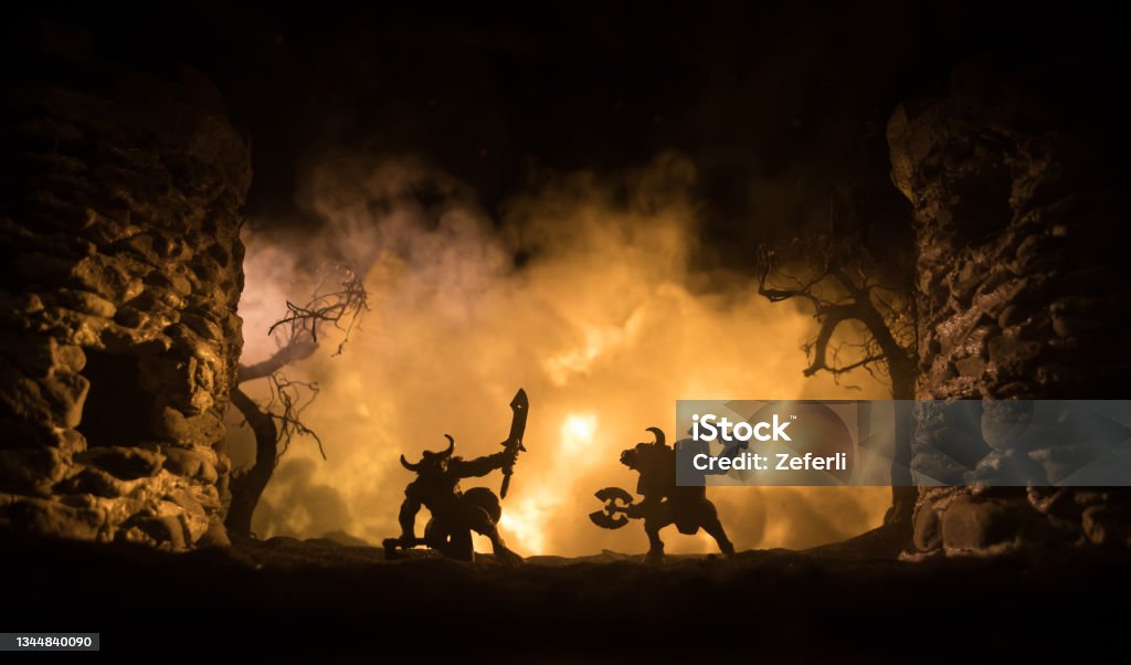 Medieval battle scene with cavalry and infantry. Silhouettes of figures as separate objects, fight between warriors on dark toned foggy background with medieval castle. Medieval battle scene with cavalry and infantry. Silhouettes of figures as separate objects, fight between warriors on dark toned foggy background with medieval castle. Selective focus Orc Stock Photo