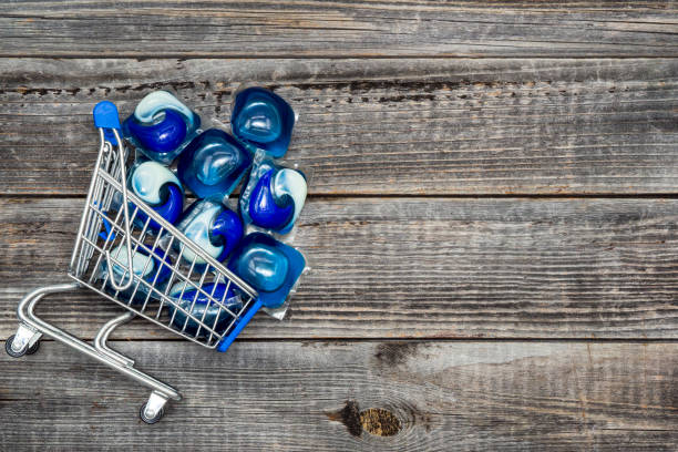 Purchase pods washing A lot of three-in-one gel capsules for wash in a washing machine in the shopping cart on a gray wooden table background. Concept laundry cleaning service. Copy space, top view. detergent capsule stock pictures, royalty-free photos & images