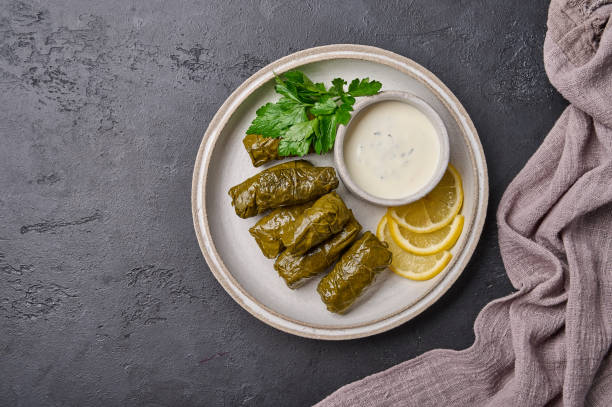 istock Dolma, stuffed grape leaves with rice, meat, sour cream and lemon on light plate 1344845433