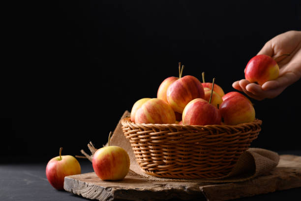 istock Red apple fruit in a basket on black background with hand, Still Life 1344846737