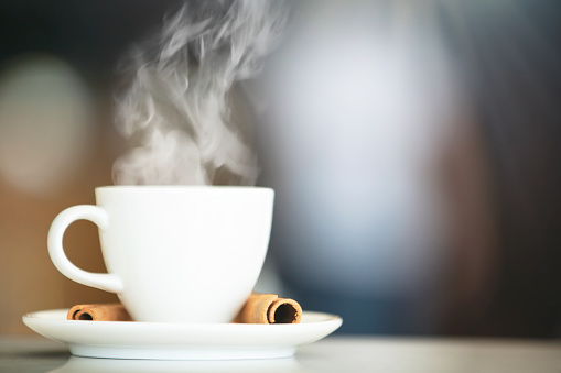 Hot cup of coffee on white desk on blurred coffee shop background