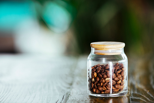 Fresh, roasted coffee beans in small jar and placed  on green wooden desk on blured indoor background