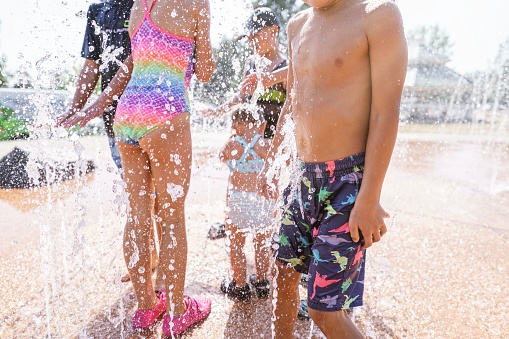 Cropped shot of a group of children playing in the fountain at an outdoor water park on a hot and sunny summer day.