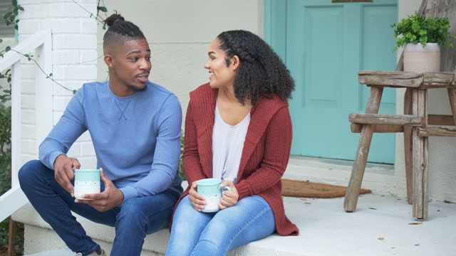 African-American couple sit on porch step, conversing