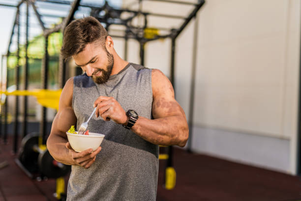 Happy young bodybuilder eating a vegetable salad.