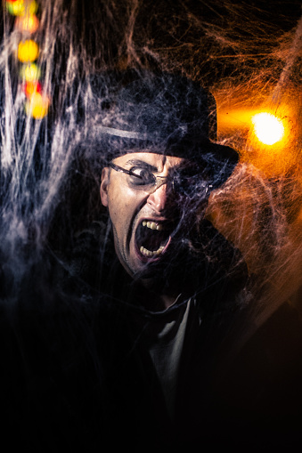 Screaming young man portrait in Vampire costume behind spider web for Halloween