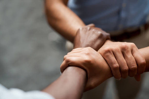 Shot of a group of businesspeople linking arms in solidarity in a modern office Work with people who pull together equality stock pictures, royalty-free photos & images