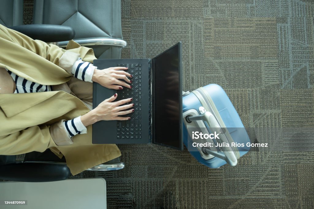 Close-up shot of unrecognizable woman working with laptop at airport next to luggage Top view of unrecognizable woman working with laptop in airport next to luggage with copy space Laptop Stock Photo