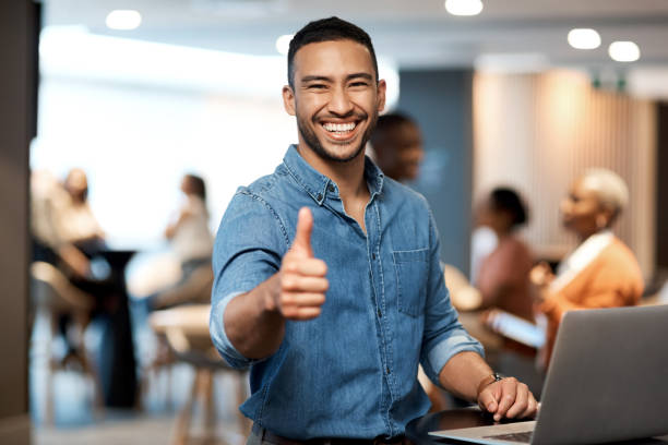 foto de un joven hombre de negocios mostrando pulgares hacia arriba mientras usa una computadora portátil en una conferencia - twenty first fotografías e imágenes de stock